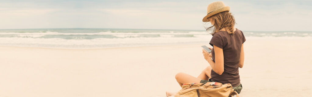 A woman sits on the beach with her phone